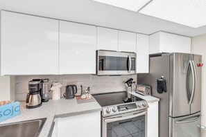 A modern kitchen with white cabinets, a stainless steel refrigerator, a microwave, a stove, and a coffee maker. - H-247 - Second Floor With Lake and Fountain View (Naples)