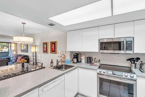 A modern kitchen with white cabinets, a stainless steel microwave, a gas stove, and a coffee maker. - H-247 - Second Floor With Lake and Fountain View (Naples)