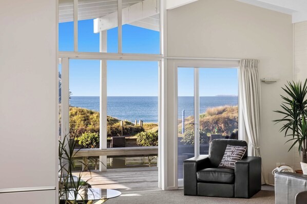 A room with a large sliding glass door leading to a balcony with a view of the sea and hills. - Beachfront Retreat Su (Mount Maunganui)