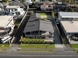 An aerial view of a residential area with a prominent house featuring a large, flat roof and a covered porch area.