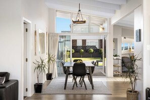 A modern dining area with a table and chairs, a chandelier, and potted plants. - Beachfront Retreat Su (Mount Maunganui)