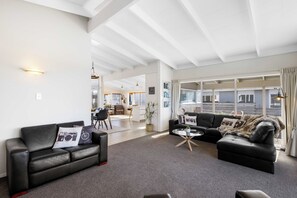 A spacious living area with a black leather sofa, a glass coffee table, and a black leather couch. There is a kitchen area in the background with a dining table and chairs.