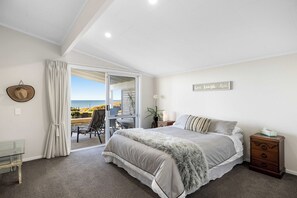 A bedroom with a bed, a nightstand, a glass table, and a view of the beach. - Beachfront Retreat Su (Mount Maunganui)