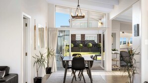 A modern dining area with a table and chairs, a chandelier, and potted plants. - Beachfront Retreat Su (Mount Maunganui)