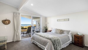 A bedroom with a bed, a nightstand, a glass table, and a view of the beach. - Beachfront Retreat Su (Mount Maunganui)