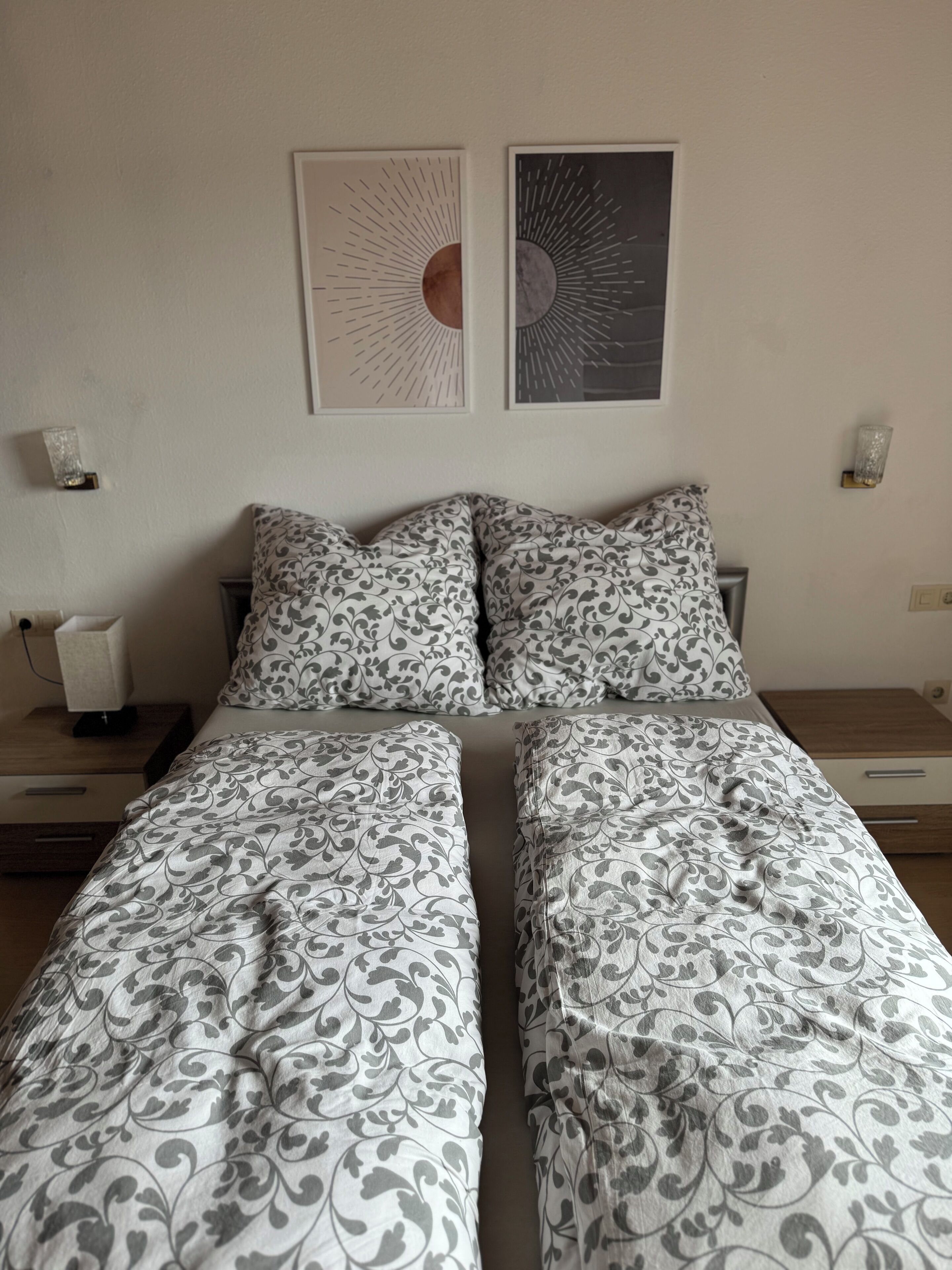 Ein Doppelbett mit gemusterten Bettbezügen, zwei Nachttische und zwei Wandlampen.