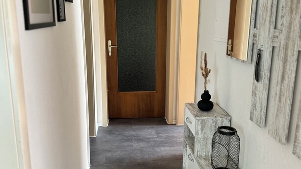 A hallway with framed pictures on the wall, a wooden door at the end, and a rustic console table with a candle and a lantern. - Vacation apartment by the vineyards, great wine hiking trails nearby (Öhringen)