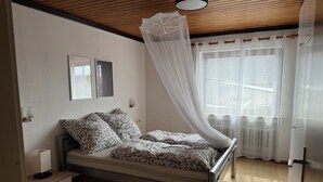 A bedroom with a bed, bedside tables, a nightstand, a window with curtains, and a ceiling fan. - Vacation apartment by the vineyards, great wine hiking trails nearby (Öhringen)