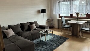 A modern living room with a grey sofa, a glass coffee table, and a dining area with a wooden table and chairs. - Vacation apartment by the vineyards, great wine hiking trails nearby (Öhringen)