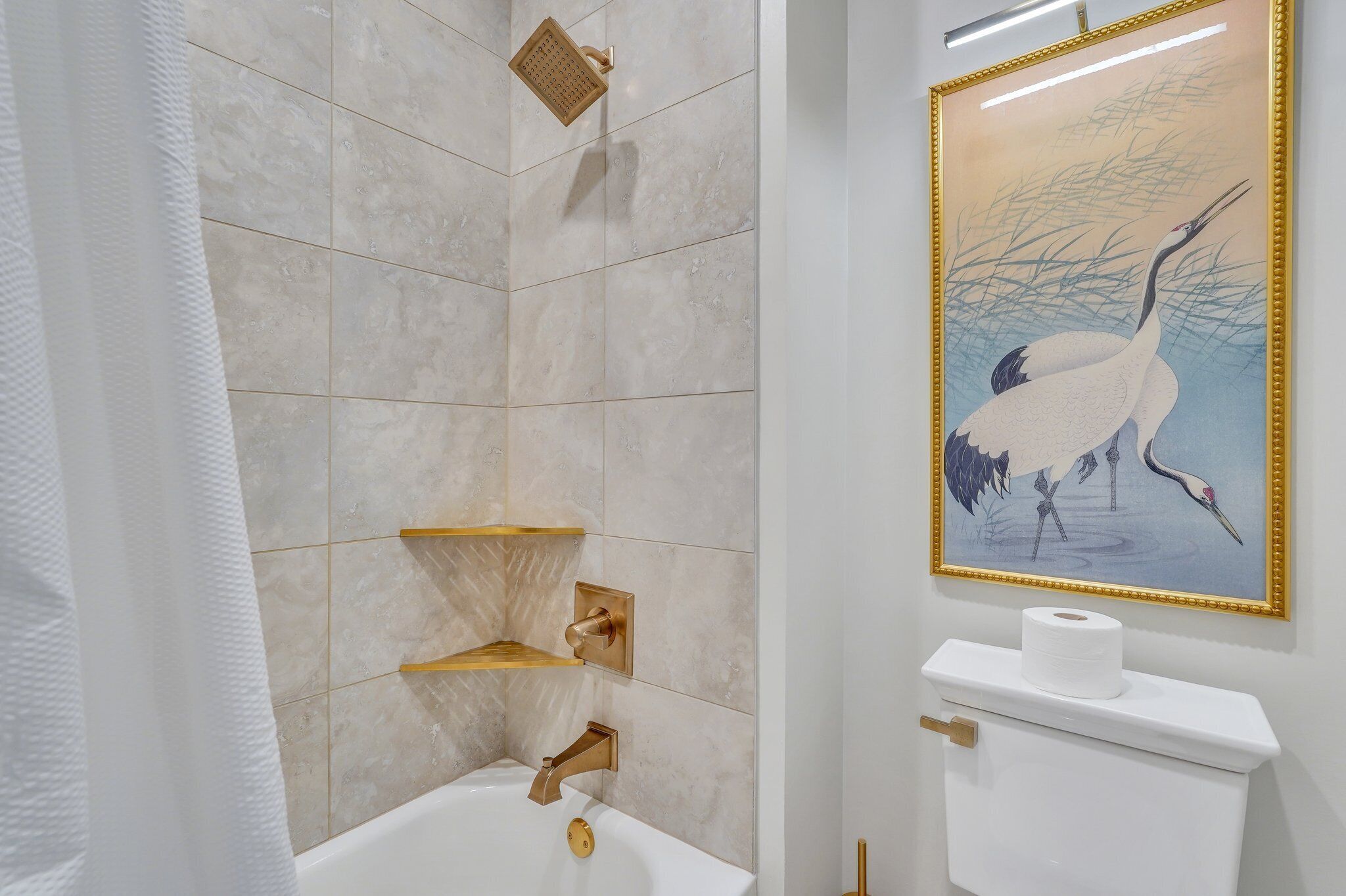 A bathroom with a white bathtub, a gold showerhead, and a toilet with a roll of toilet paper.