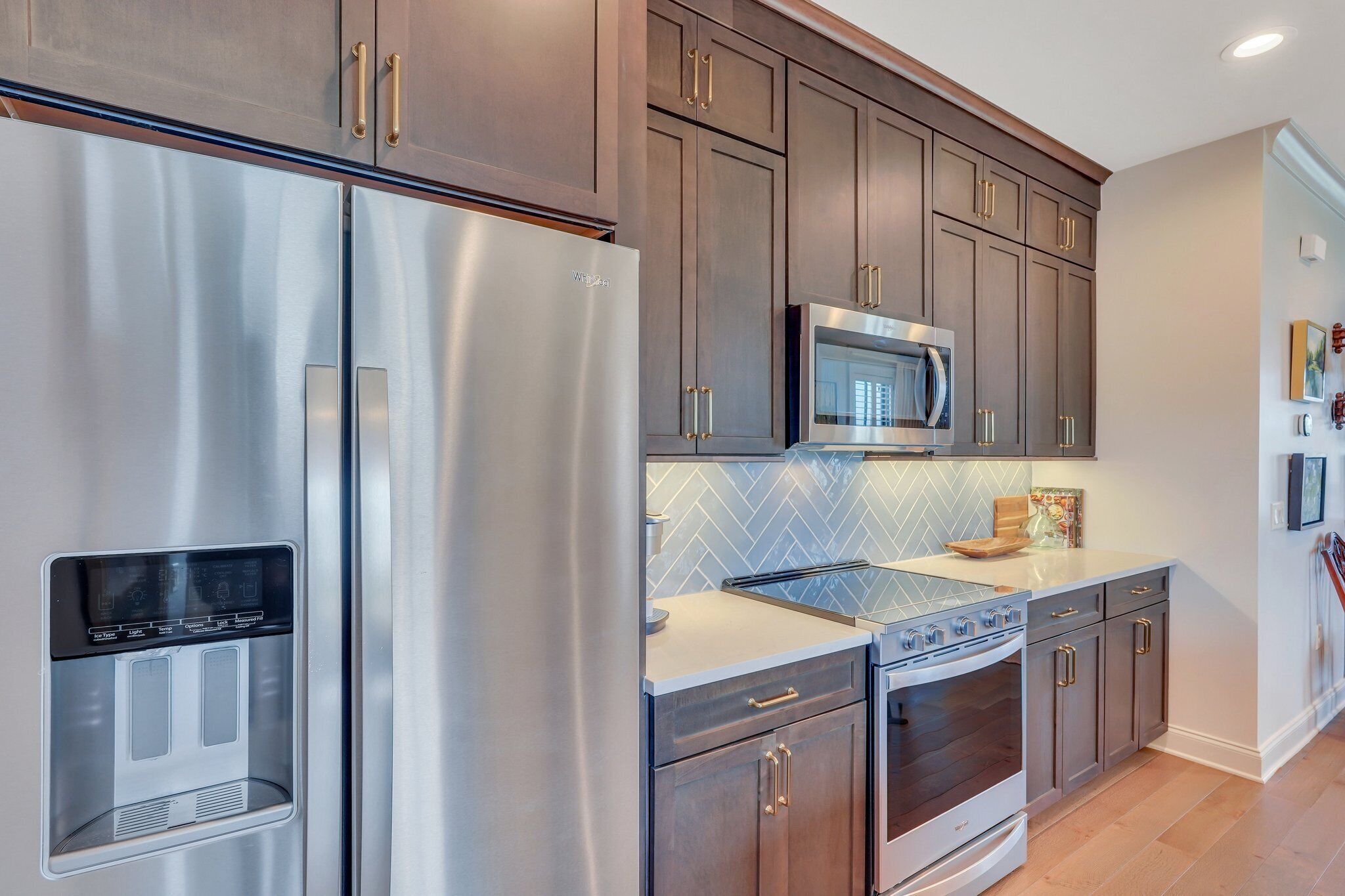 A modern kitchen with stainless steel appliances, dark wooden cabinets, and a herringbone tile backsplash.