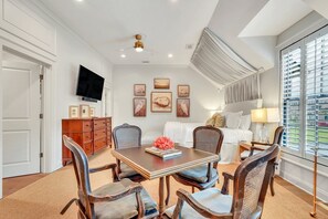 A hotel room with a dining table, chairs, a bed, a TV, artwork on the walls, and a large window with a view.
