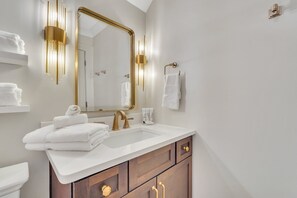 A bathroom with a white sink, gold fixtures, and a large mirror.