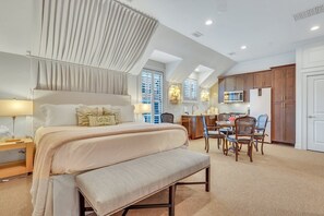 A hotel room with a large bed, a bench, a desk with chairs, a microwave, and a dining area.