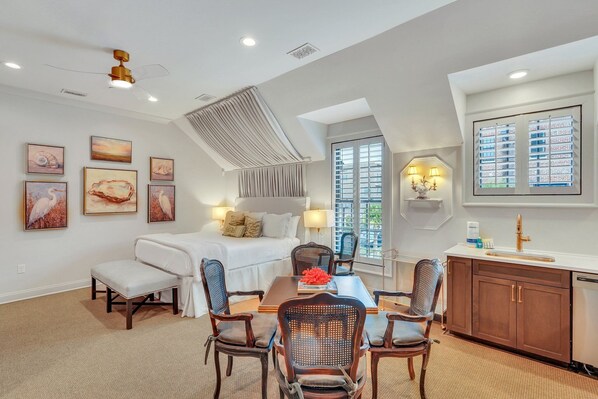 A modern hotel room with a bed, seating area, dining table, and kitchen.