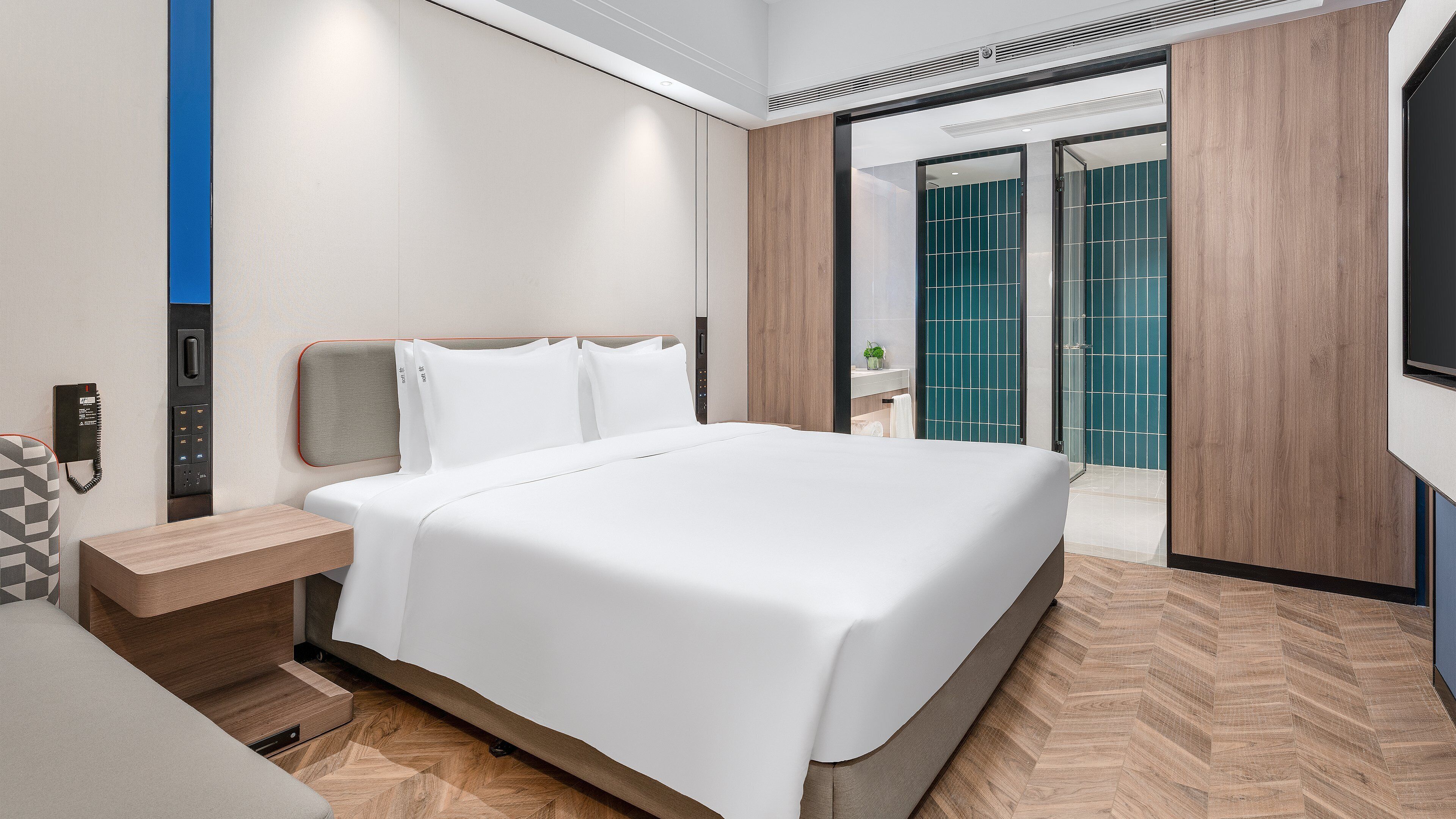 Una habitación de hotel moderna con una cama grande, una mesita de noche, un teléfono y vistas al baño.