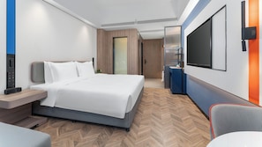 A modern hotel room with a bed, bedside table, TV, and a desk area.