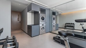 Une salle de sport moderne équipée d’un vélo d’appartement, d’un tapis de course, ainsi que d’une laveuse et d’une sécheuse fixées au mur.