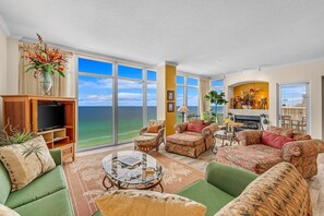 A spacious living room with a large window overlooking the ocean, furnished with green sofas, a coffee table, and a fireplace.