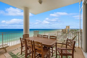 A balcony with a wooden table and chairs, overlooking a beach and ocean.