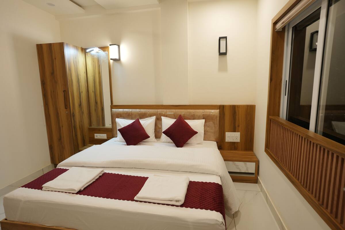 A neatly made bed with white and red bedding, a wooden headboard, and a window with blinds.