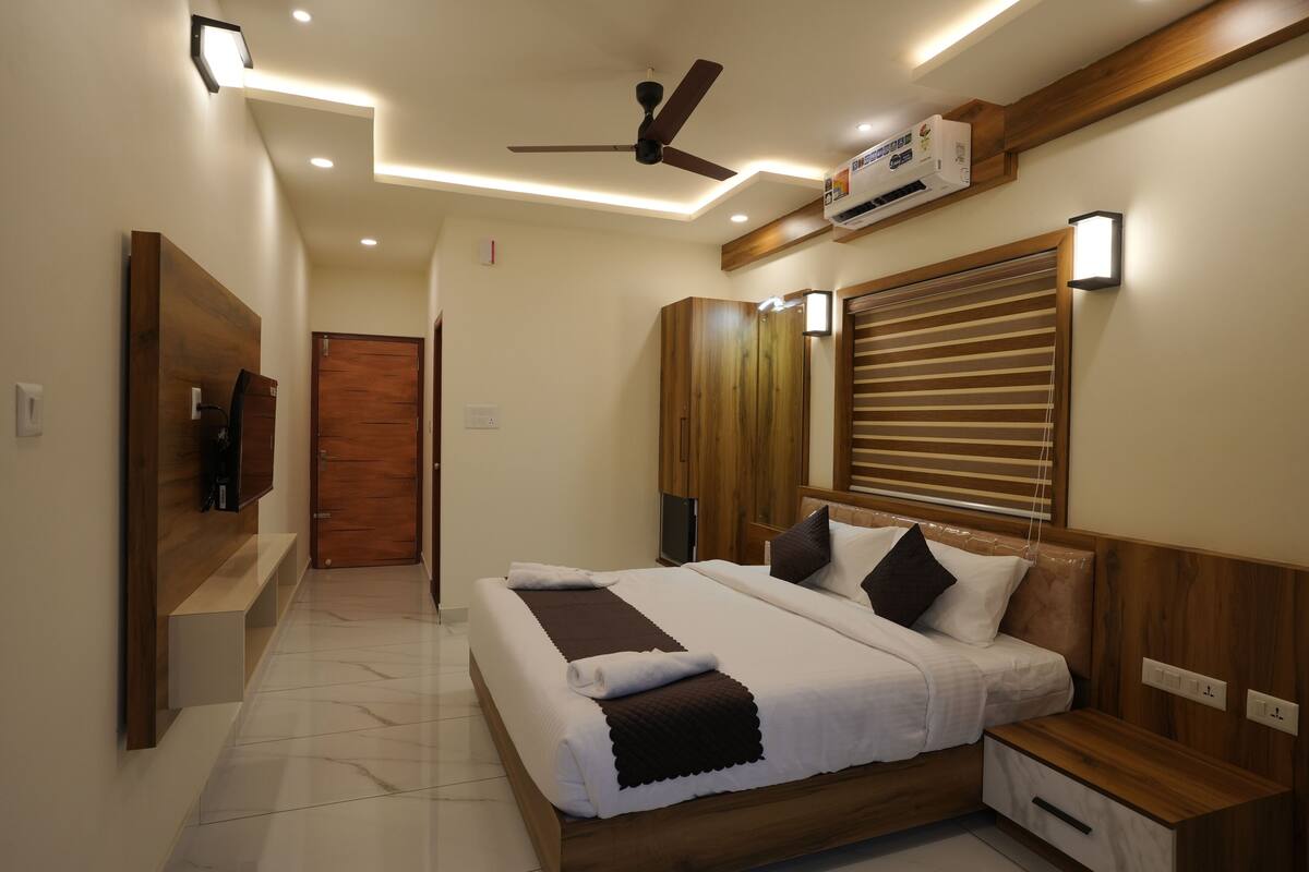 A modern hotel room with a large bed, wooden headboard, bedside tables, and a ceiling fan.