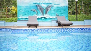 A swimming pool with two lounge chairs and a mural of dolphins.