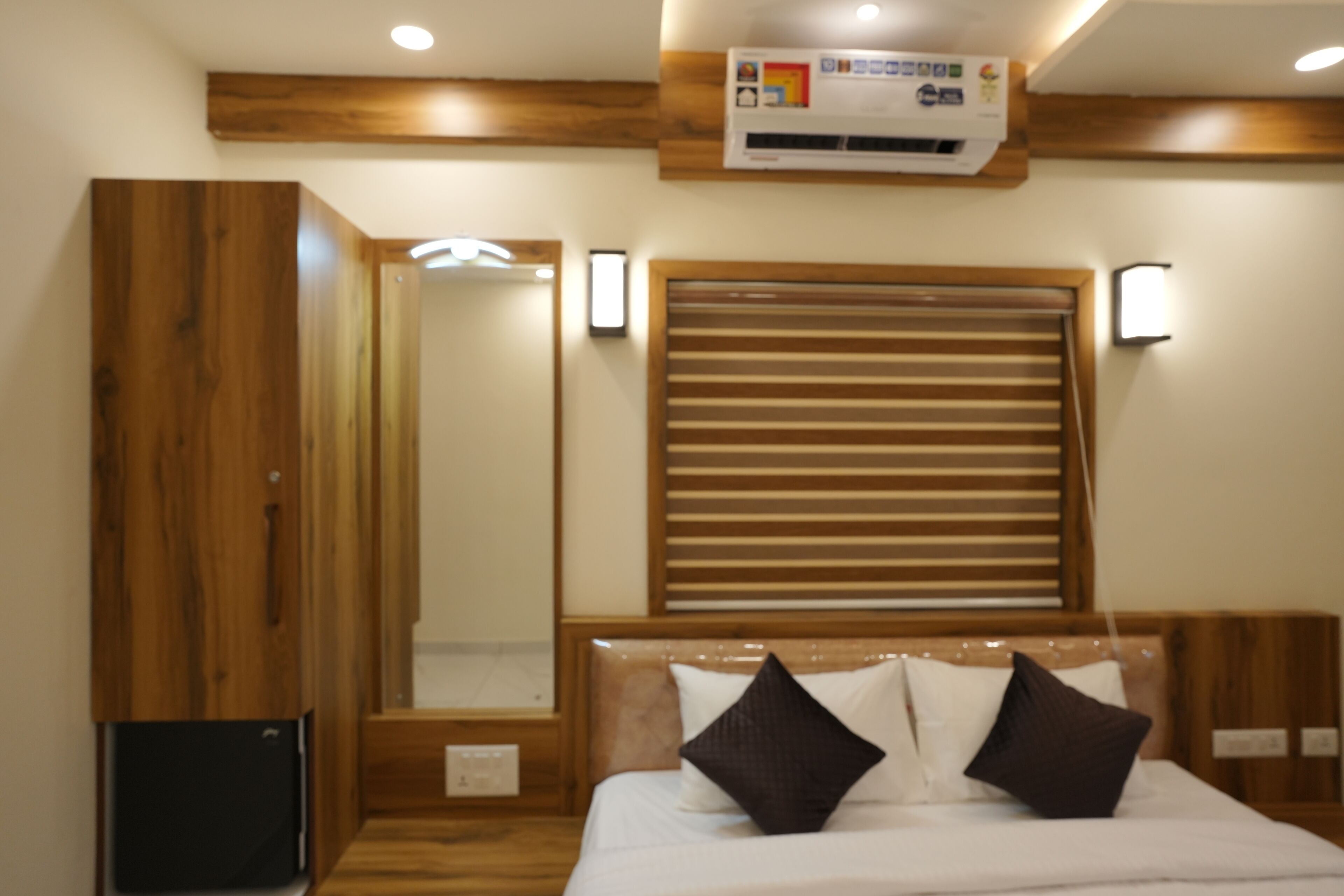 Een slaapkamer met een houten hoofdbord, een bed met witte beddengoed en twee donkere kussens, een houten garderobe en een ingebouwde airconditioning.