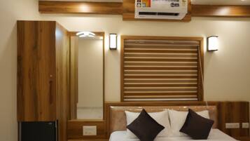Een slaapkamer met een houten hoofdbord, een bed met witte beddengoed en twee donkere kussens, een houten garderobe en een ingebouwde airconditioning.