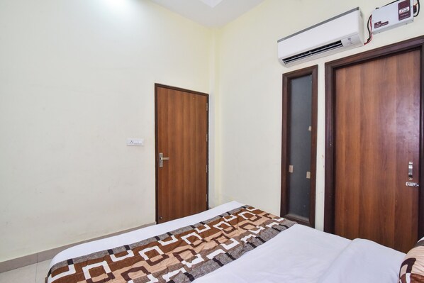 A bedroom with a bed, a patterned blanket, a wooden wardrobe, and an air conditioning unit. - HOTEL SK PLAZA (Amritsar)