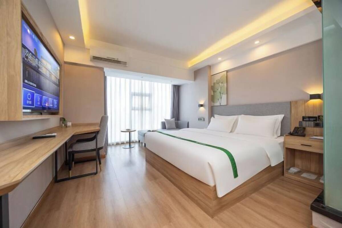 A hotel room with a bed, a desk, a chair, a TV, and a window.