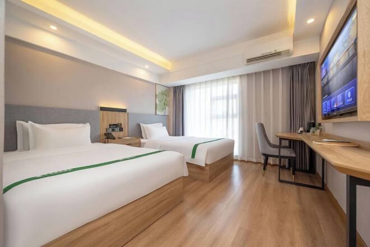 A hotel room with two beds, a desk, a chair, a TV, and a window with curtains.