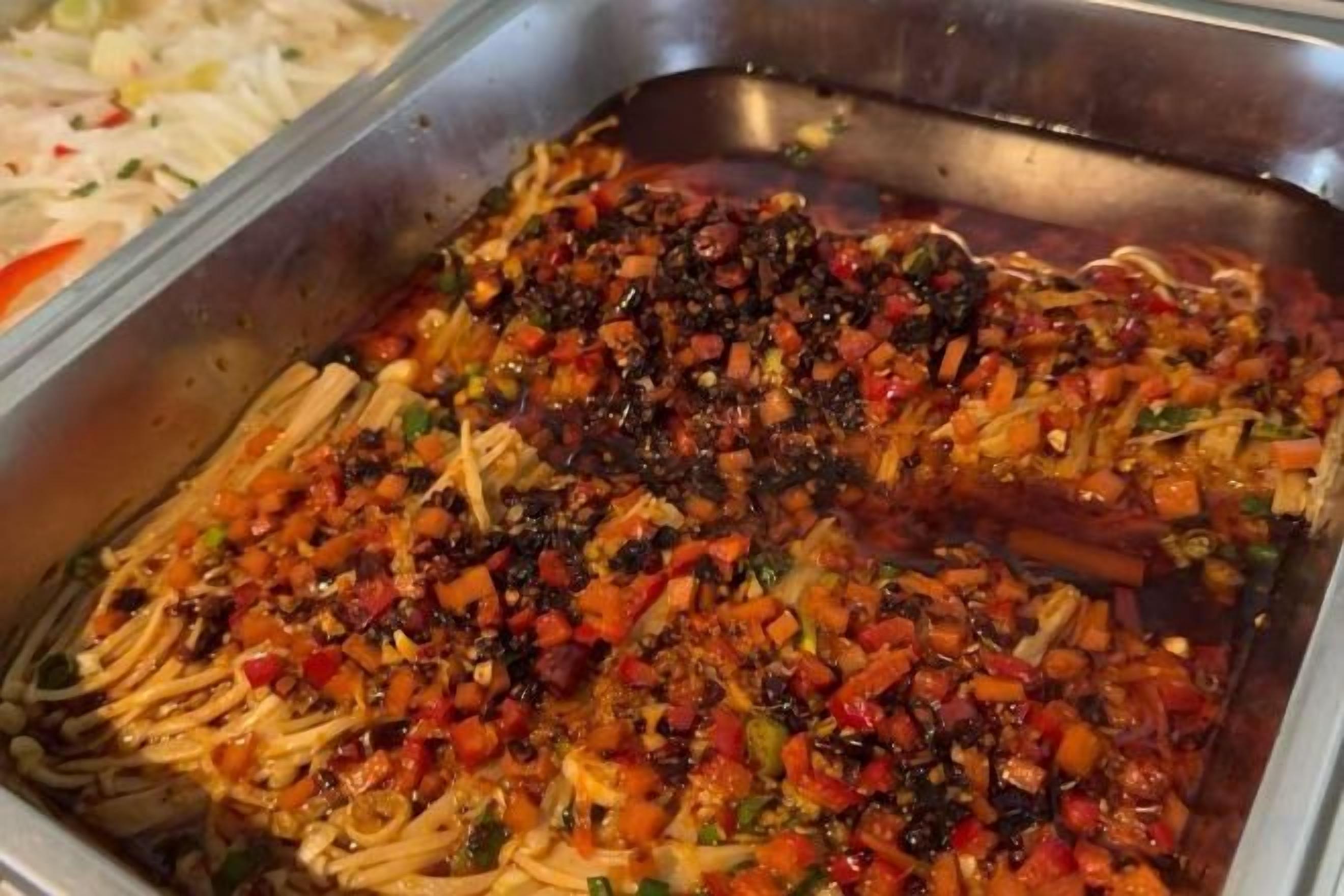 Un bufé con diversos platos, incluyendo un plato de fideos con verduras y salsa roja.