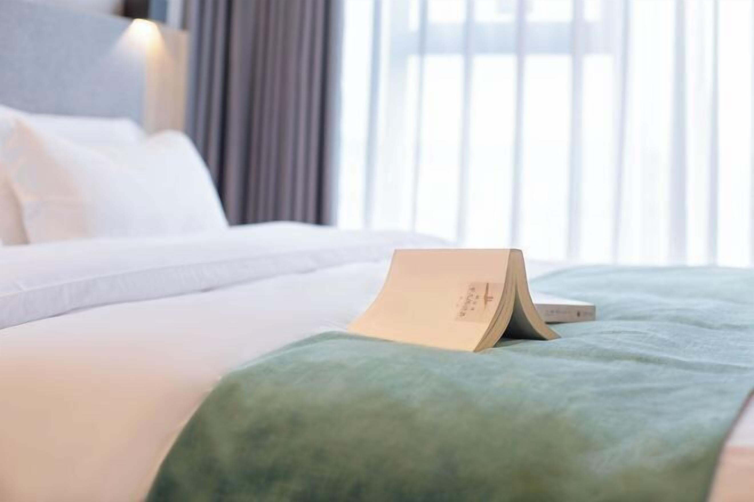 A neatly made bed with a green blanket and a folded card on it.