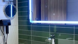 A bathroom with a green tiled wall, a round mirror, a white sink, and a hairdryer on a stand. - Greentree Inn Express Deyang Changjiang Dong Road (Deyang)