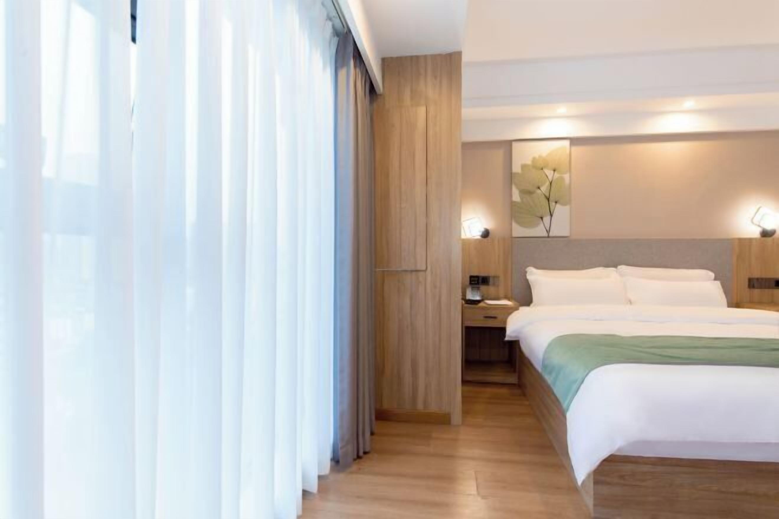 Een moderne hotelkamer met een houten vloer, een groot bed met witte lakens, een bureau met een lamp en een kunstwerk aan de wand.