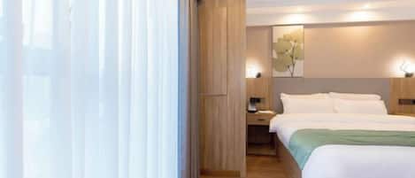 Una habitación de hotel moderna con piso de madera, una cama grande con ropa blanca, un escritorio con lámpara y una obra de arte colgada en la pared.