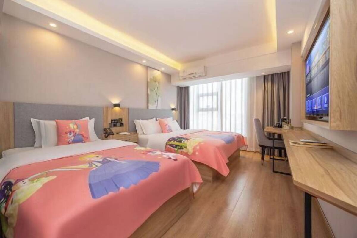 A hotel room with two beds, a desk, and a TV.