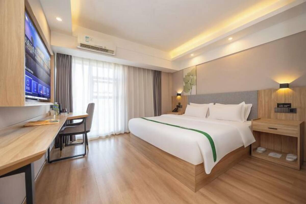 A hotel room with a bed, a desk, a chair, a TV, and a window with curtains.