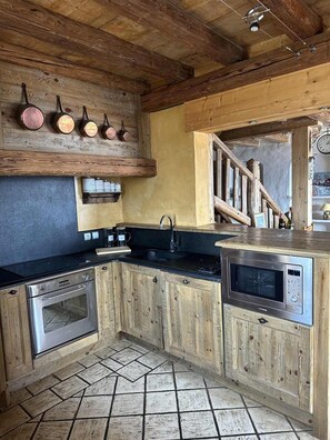A rustic kitchen with wooden cabinets, a black countertop, a stainless steel oven, a microwave, and a hanging pot rack. - Chalet, 100m from ski slopes, hammam, terrace, fireplace or stove, tv, 210m², Les Saisies (Villard-sur-Doron)