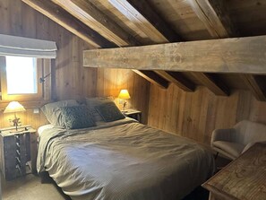 A cozy wooden cabin bedroom with a bed, two bedside lamps, a chair, and a window with a curtain. - Chalet, 100m from ski slopes, hammam, terrace, fireplace or stove, tv, 210m², Les Saisies (Villard-sur-Doron)