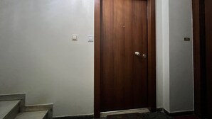 Een houten deur met een deurklink en sleutelgat, een lichtschakelaar en een klein rechthoekig object aan de muur.