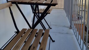 Een houten tafel en bankjes op een balkon met een leuning, een bloempot en een witte mand.