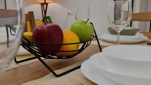Een eettafel met een fruitmand met appels en sinaasappels, een wijnglas en een wit bord.