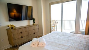 Habitación de hotel con cama, cómoda de madera, televisor de pantalla plana y balcón con una silla.