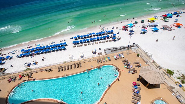 Vista aérea de un resort con una gran piscina, playa con tumbonas y una zona de piscina separada.
