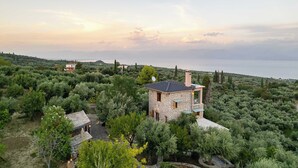 A stone house with a flat roof surrounded by dense greenery and a view of the sea. - Stone Farmhouse in Groves - Sea & Mountain Views (Achladochori)