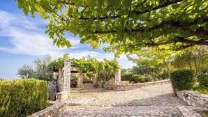 A stone pathway leading to a stone structure with a pergola, surrounded by greenery and a clear sky. - Stone Farmhouse in Groves - Sea & Mountain Views (Achladochori)