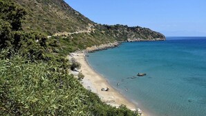 A coastal landscape with a sandy beach, clear blue water, and a rocky hillside. - Stone Farmhouse in Groves - Sea & Mountain Views (Achladochori)