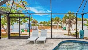 Un espacio al aire libre cubierto con piscina, sillas de descanso y vistas a edificios residenciales.